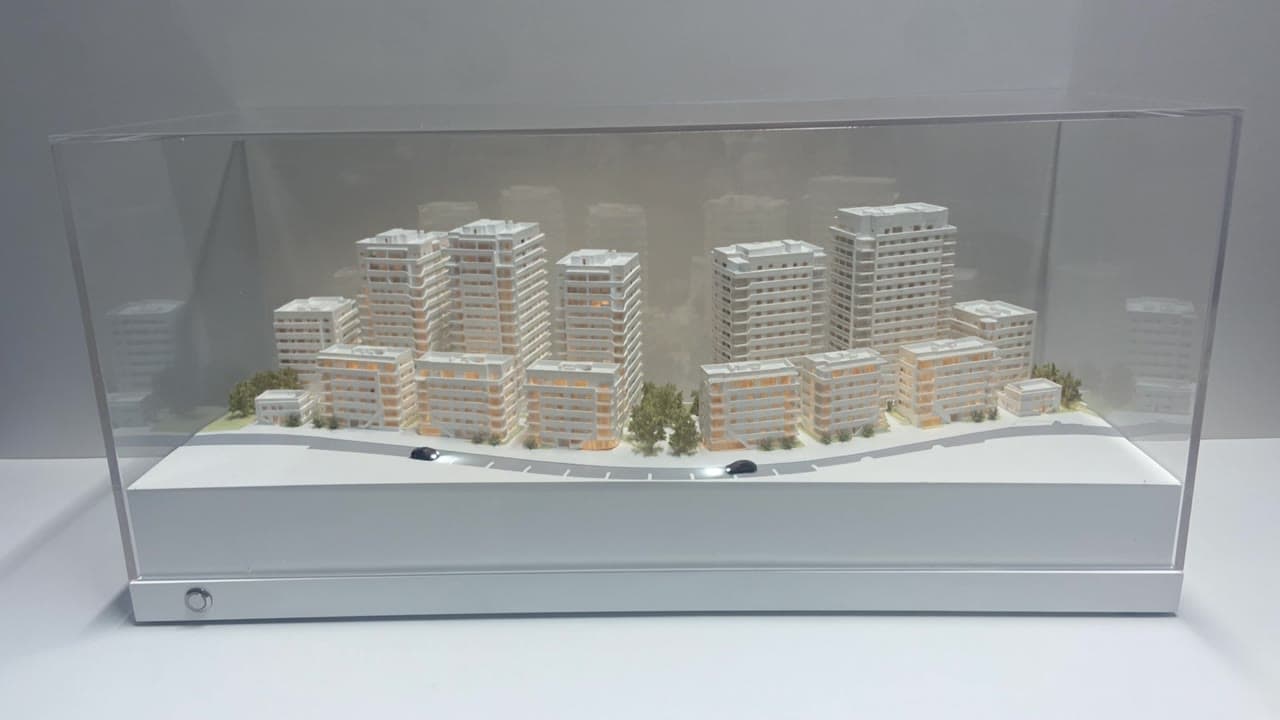 מודל אדריכלי בקנה מידה של פרויקט מגורים על בסיס תצוגה, המדגים את היחס בין המבנים לסביבה